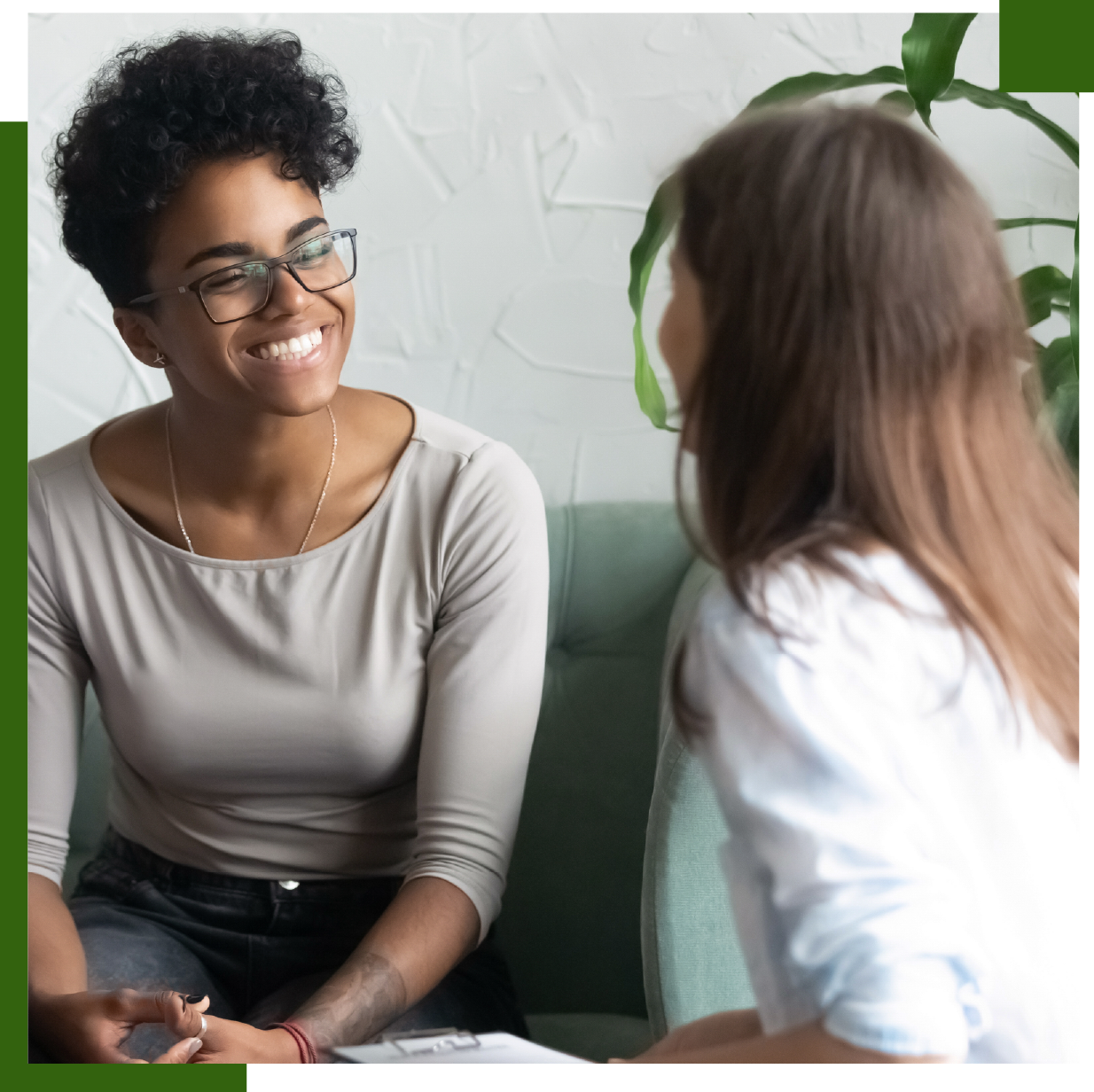 Woman smiling during a counseling session. She is sitting on a sofa and looking at the counselor, who holds a clipboard.