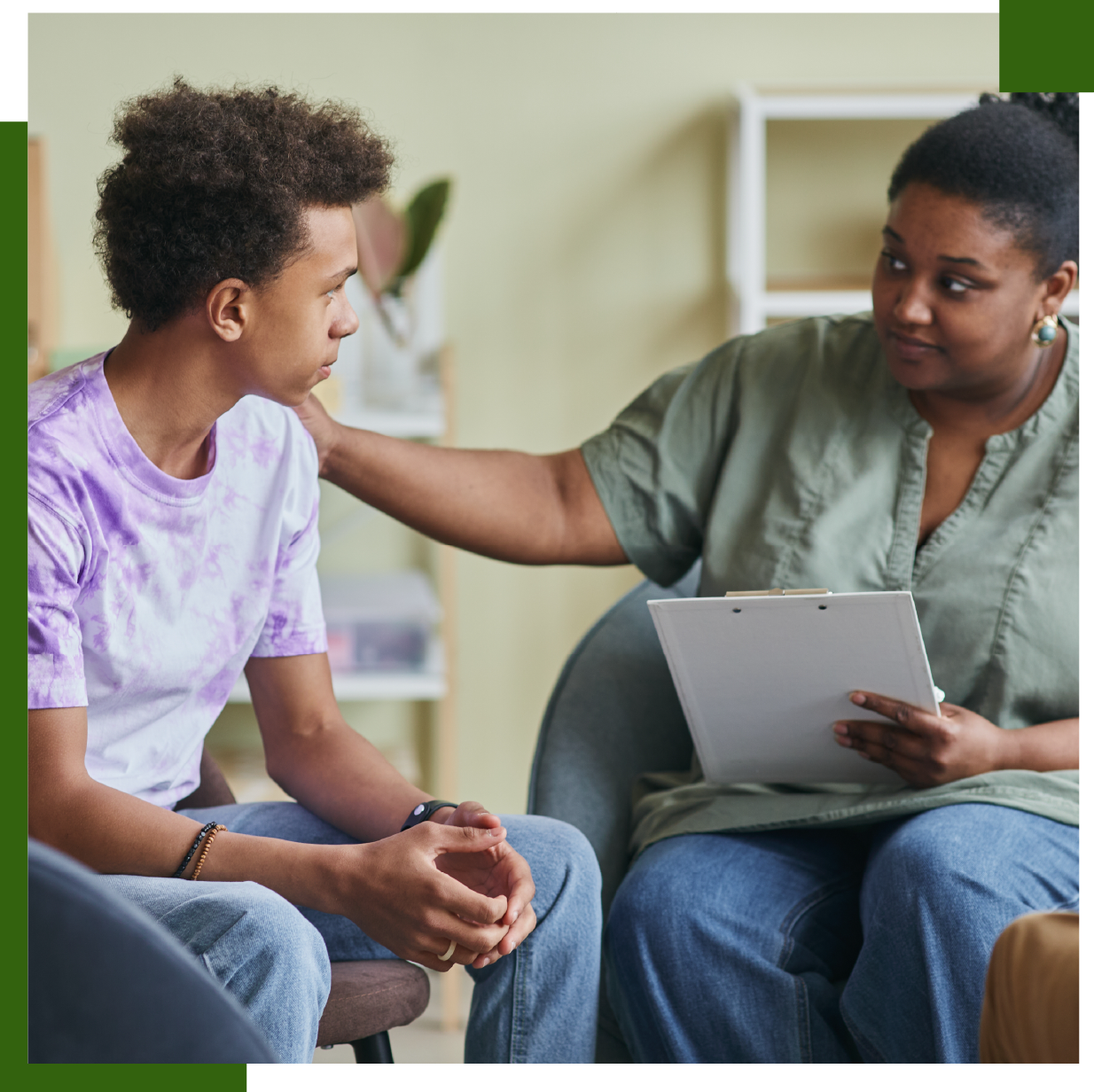 Teenager in a therapy session; therapist comforts him with a hand on his shoulder.