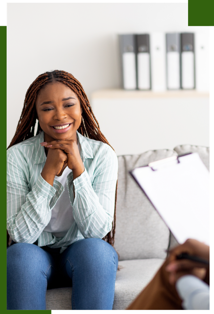 Woman smiling, hands clasped, sits on a couch in therapy session.
