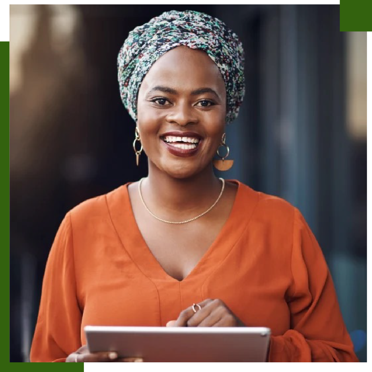 Woman wearing a patterned head covering and orange shirt, holding a tablet and smiling.