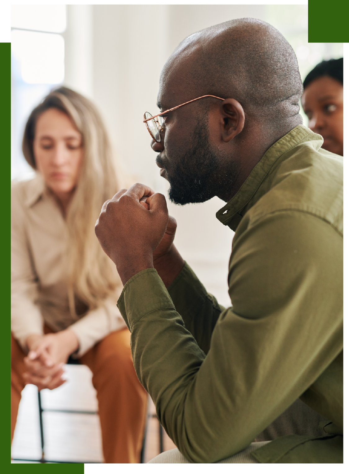 Man with glasses and clasped hands listening in a group therapy session.