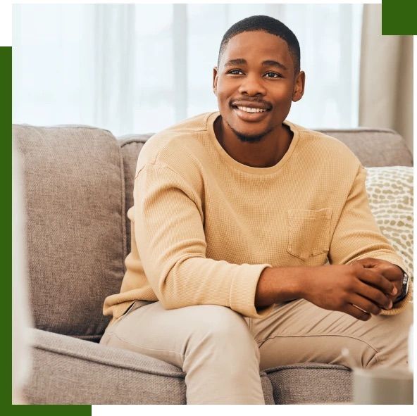 Man sitting on a gray sofa smiling indoors.