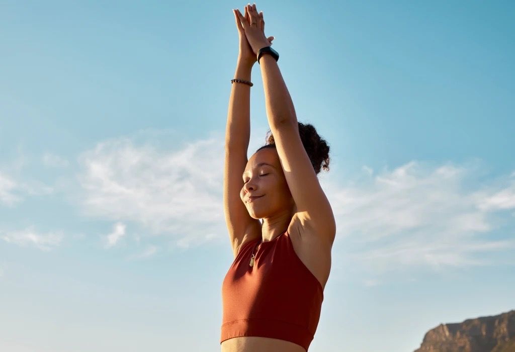 Woman with arms raised, eyes closed, doing yoga outdoors.