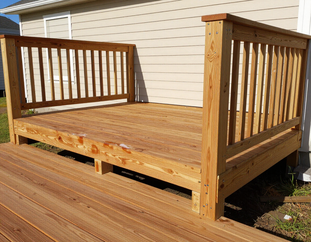 Wooden outdoor deck with railings beside a beige house, seen in bright sunlight