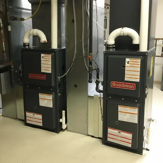 Two Goodman furnaces with white vent pipes in a utility room.