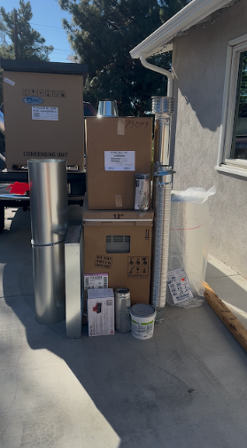 Boxes and metal parts stacked outside a building, likely construction or installation materials.
