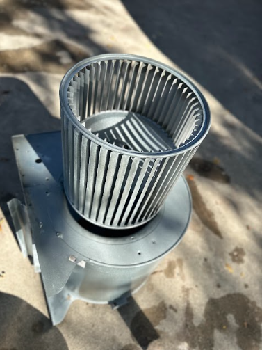 Blower assembly: gray metal fan and housing, outdoors on a concrete surface.