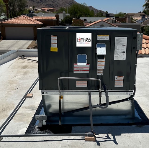 Rooftop HVAC unit with Compass logo on a flat roof, residential neighborhood in the background.