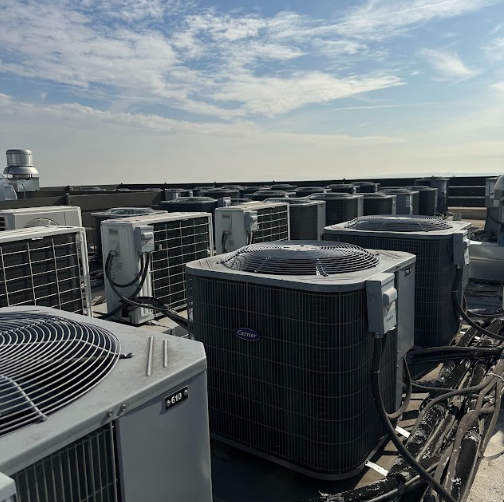 Rooftop with numerous air conditioning units against a cloudy sky.