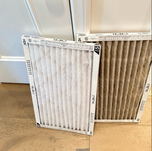 Two rectangular HVAC air filters: one clean white, one dirty brown, sitting on a wooden floor.