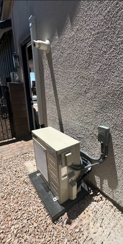 Outdoor AC unit against a stucco wall, with a supporting pole and electrical conduit.