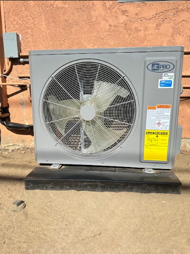 Gray air conditioning unit with fan against an orange wall.