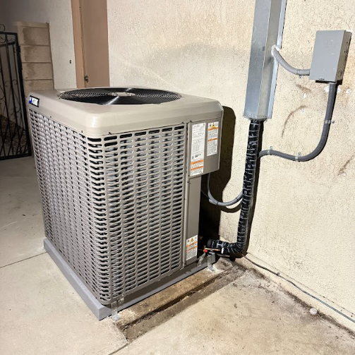 Air conditioning unit next to a stucco wall, with electrical conduit and a gray box.