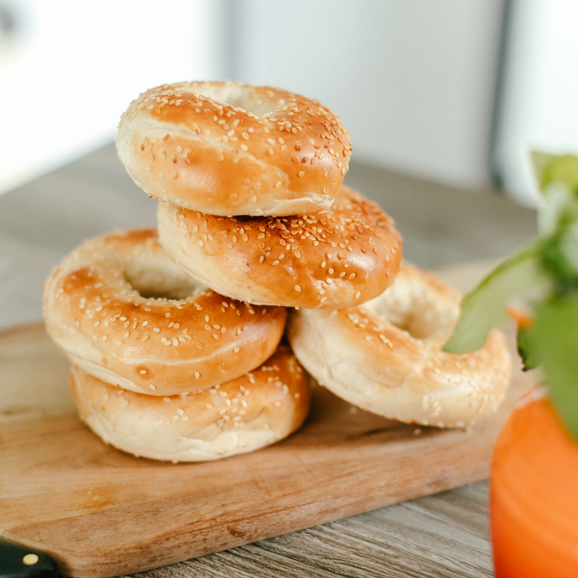 Stack of sesame seed bagels on a wooden cutting board.