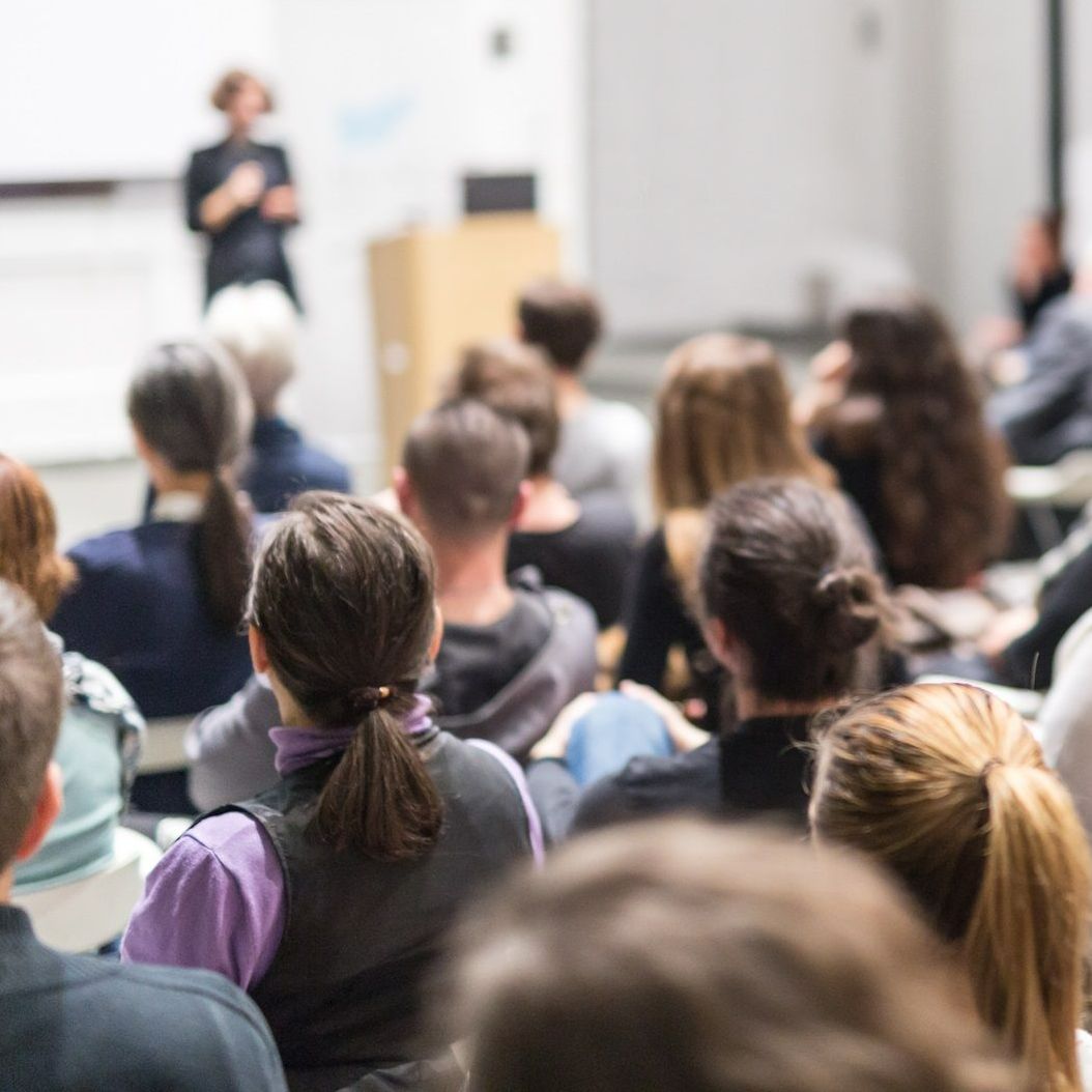 A group of people are sitting in a lecture hall listening to a presentation.
