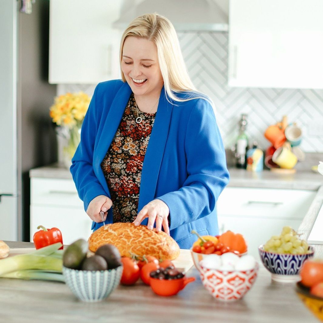 A woman in a blue jacket is cutting bread in a kitchen