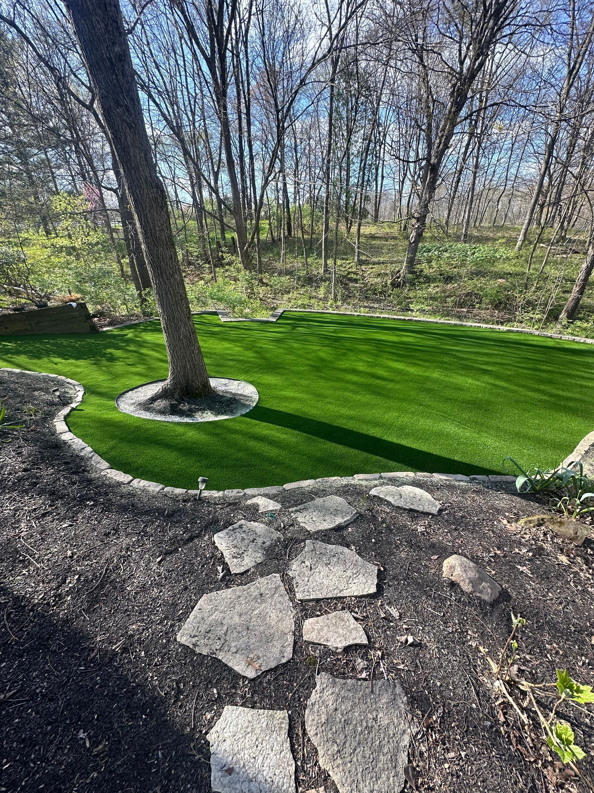 A lush green lawn with a tree in the middle of it surrounded by trees and rocks.
