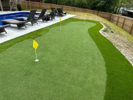 There is a putting green in the backyard next to a pool.