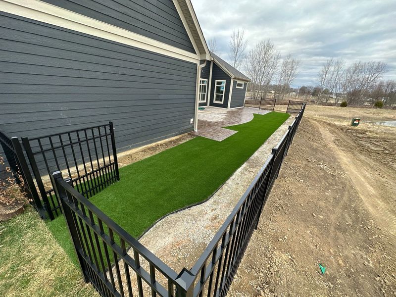 A black fence surrounds a lush green lawn in front of a house.
