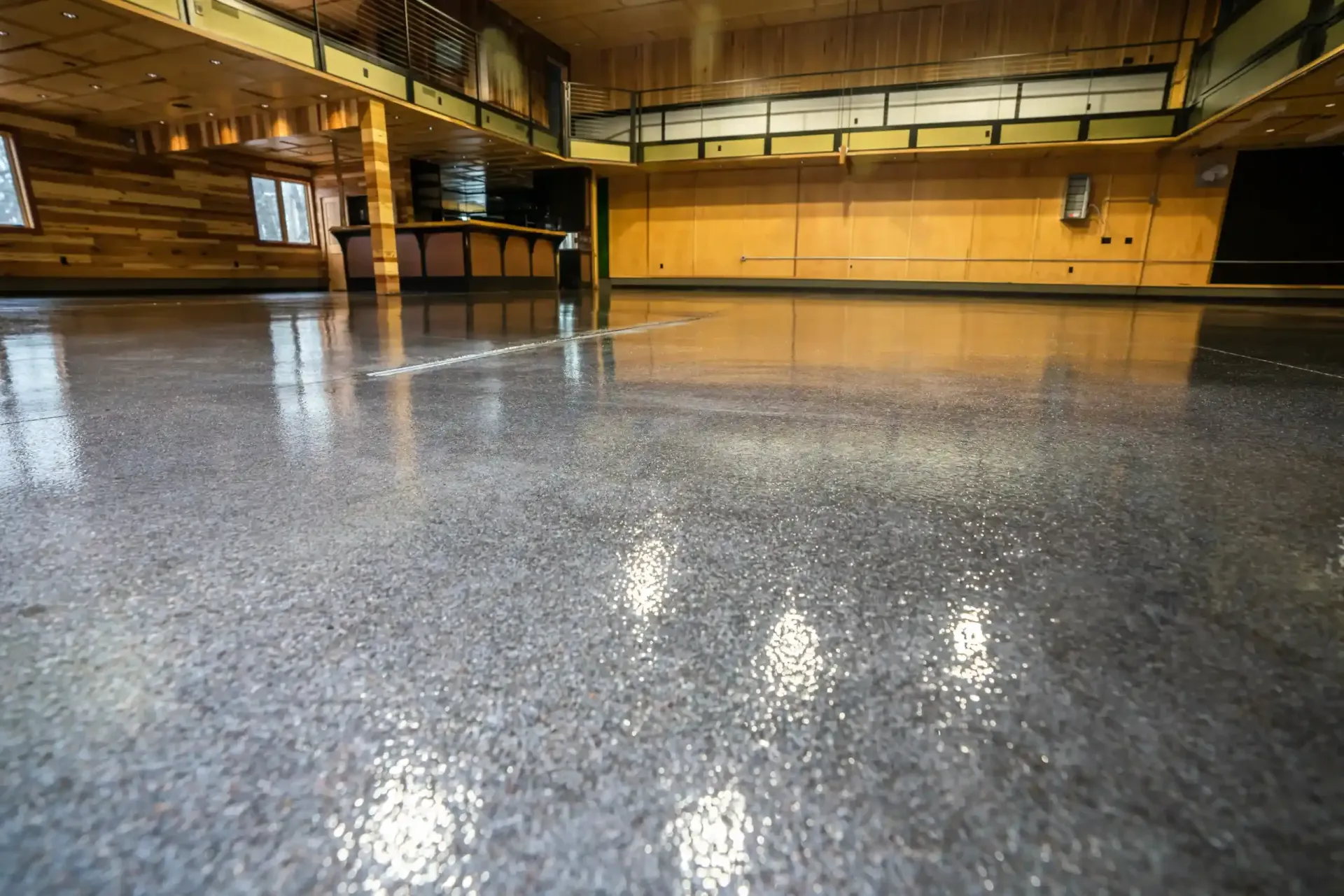 A wide, polished gray concrete floor with a glossy finish reflecting ceiling lights in an open commercial interior.