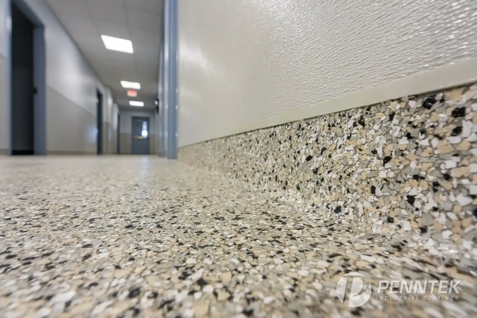 A perspective view of a hallway featuring a mottled gray and tan epoxy floor and matching curved wall base.