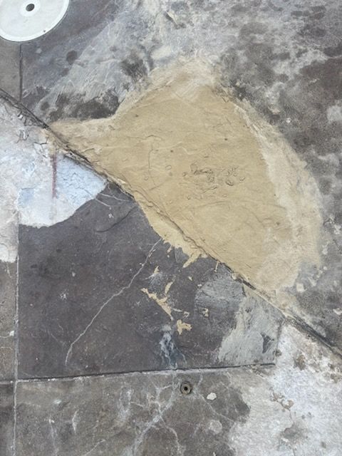Damaged concrete floor with a beige patch over dark gray and white tiles.