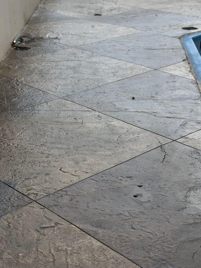 Wet stone-tiled walkway beside a blue-edged pool, with puddles and scattered debris.