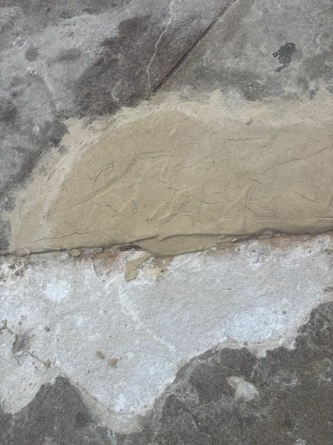 Cracked stone wall with a beige patch over white and gray concrete.