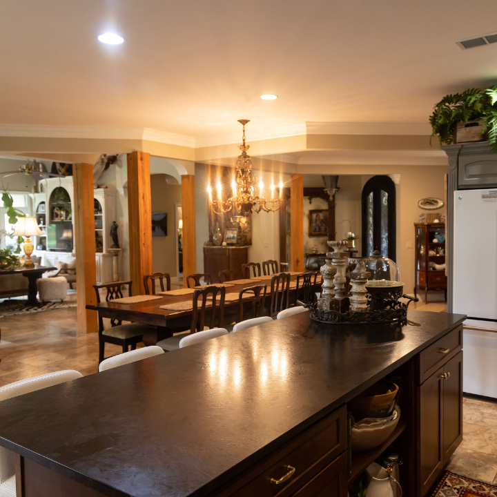 A kitchen island with a dark countertop sits in the foreground of an open-concept dining room with a chandelier.