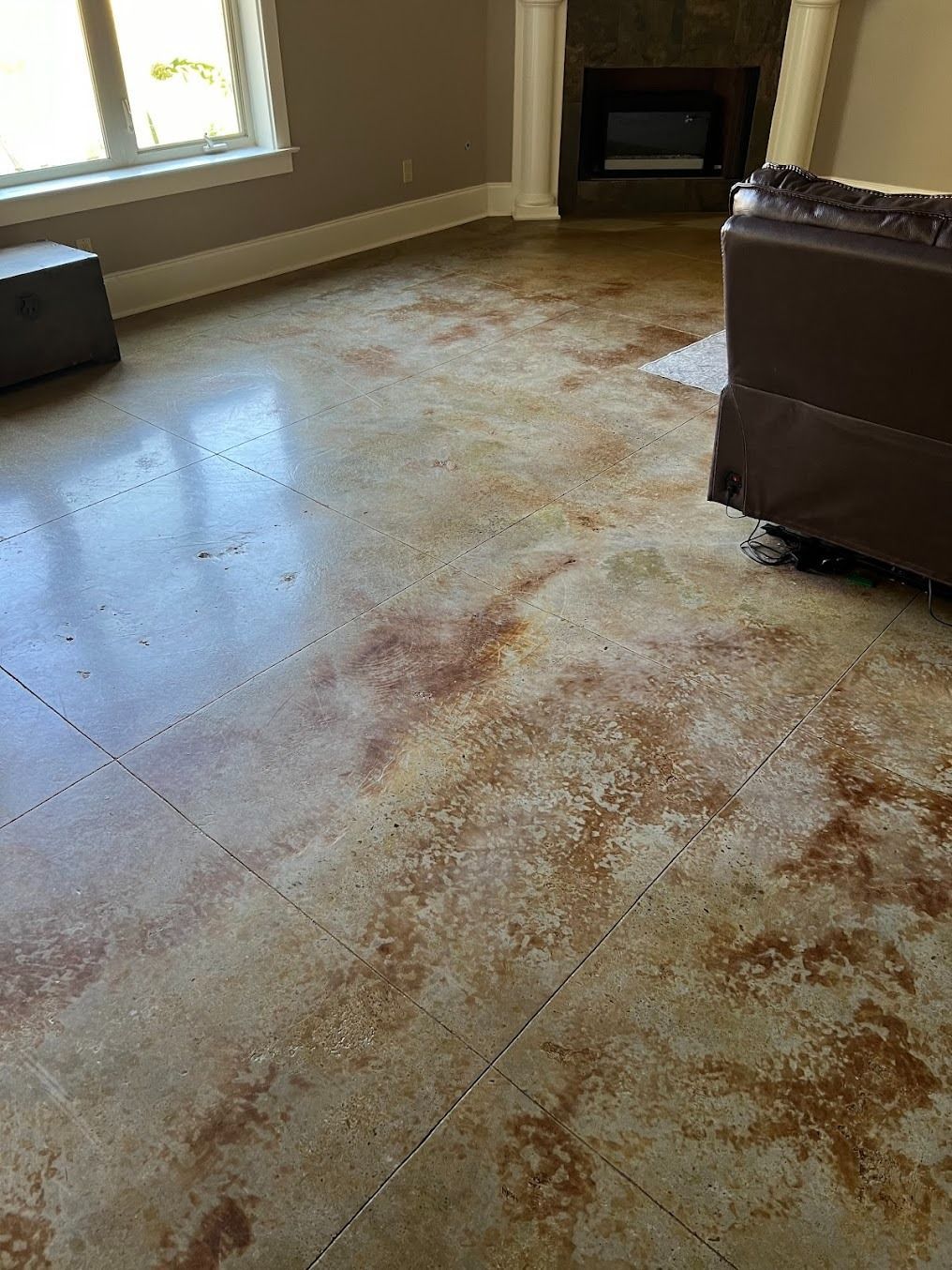 A living room interior featuring a polished concrete floor with a mottled, tan and brown rustic stain finish.
