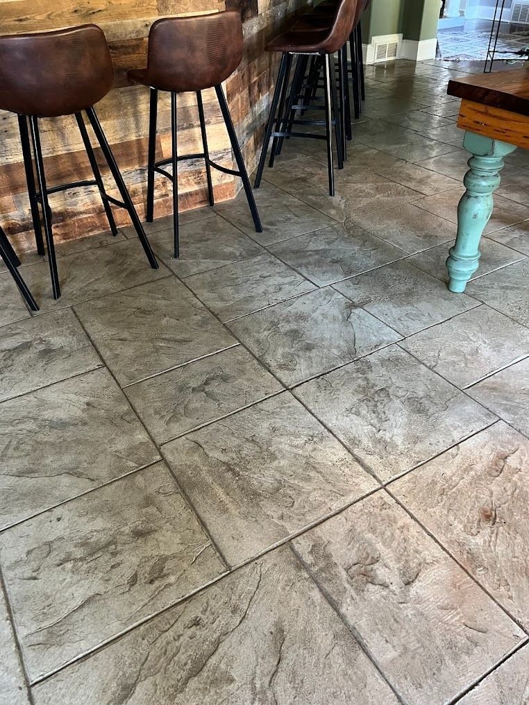 Three brown bar stools lined up against a wooden bar on a textured, light gray tiled floor.