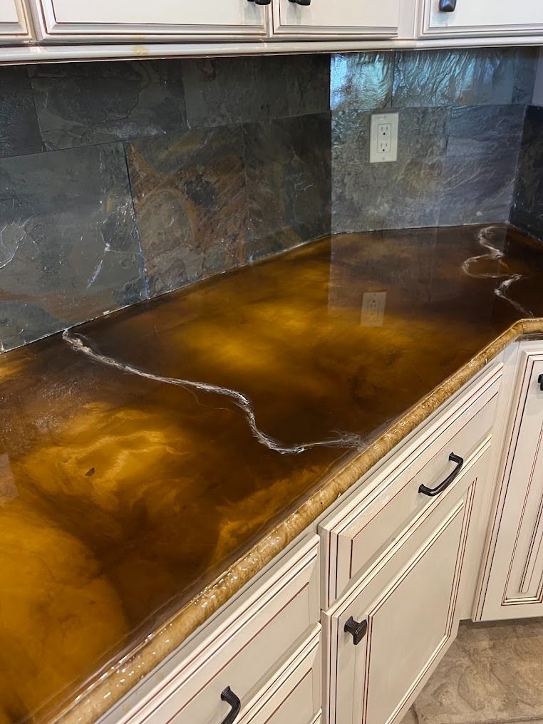 A kitchen countertop with a glossy, marbled brown epoxy finish, featuring white vein accents against stone backsplash.