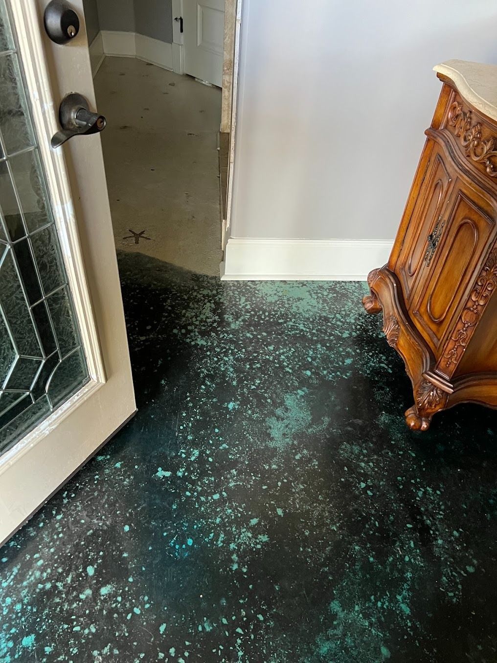 A floor with black epoxy and teal speckles, situated near a door and a wooden cabinet with a marble top.