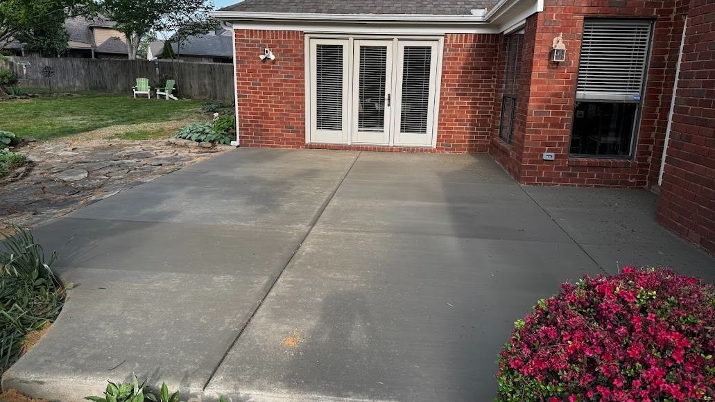 A concrete patio outside a brick house with a set of glass-paned double doors and a window with white shutters.