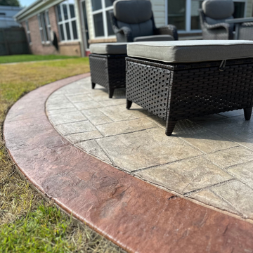 A rounded stamped concrete patio border in reddish-brown, surrounding a lighter textured tile patio with outdoor seating.