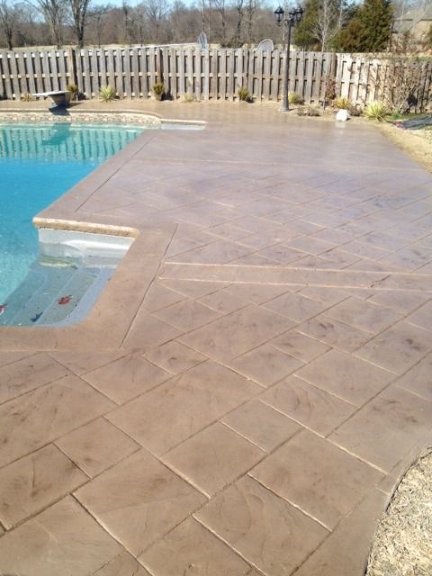 A swimming pool bordered by a textured, tan-colored stamped concrete deck with a diagonal stone pattern.
