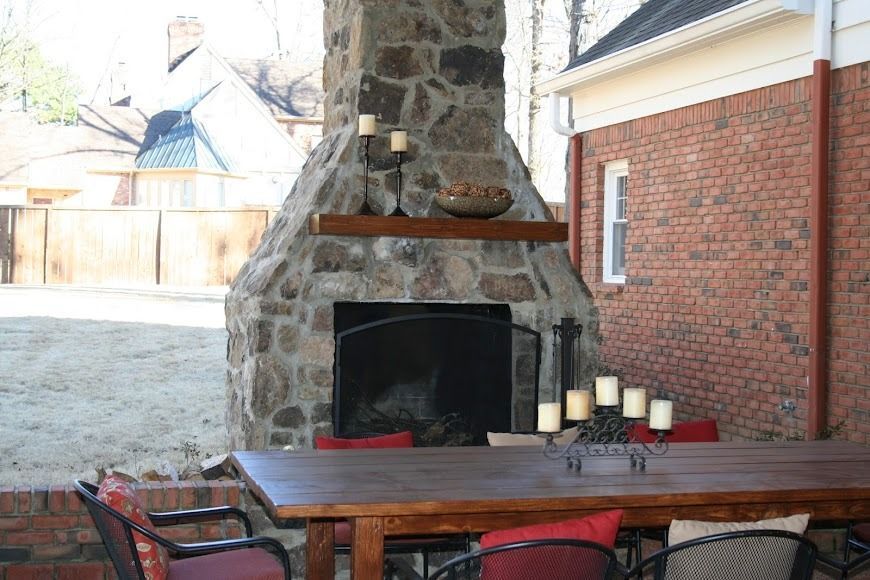 Outdoor stone fireplace and a rustic wooden dining table on a brick patio.