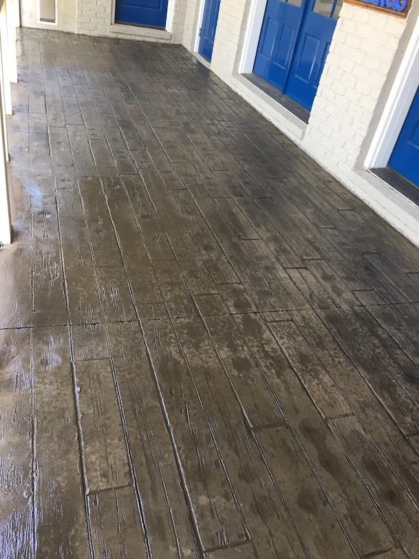 A wooden-textured concrete porch with blue doors along a white brick building.