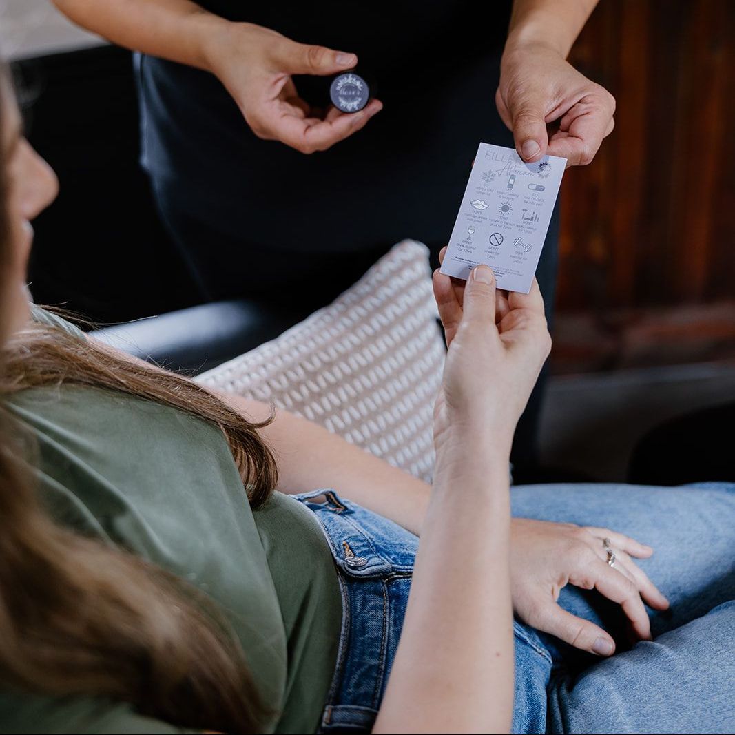 A woman is sitting in a chair holding a card and a bottle of pills.