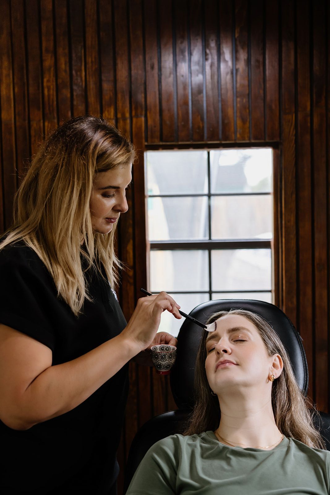 A woman is applying chemical peel to another woman 's face.