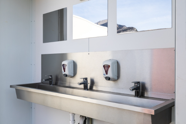 Un évier en acier inoxydable avec trois robinets et distributeurs de savon dans une salle de bain.