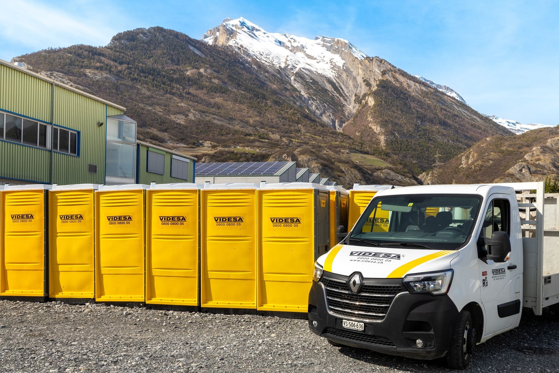 Une camionnette blanche est garée à côté d'une rangée de toilettes portables jaunes.