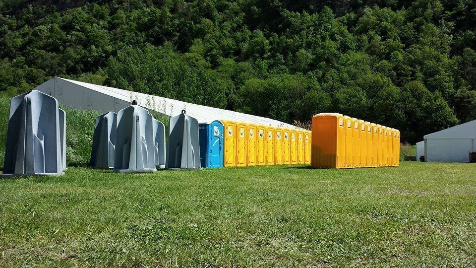 Une rangée de toilettes portables est alignée dans un champ herbeux.