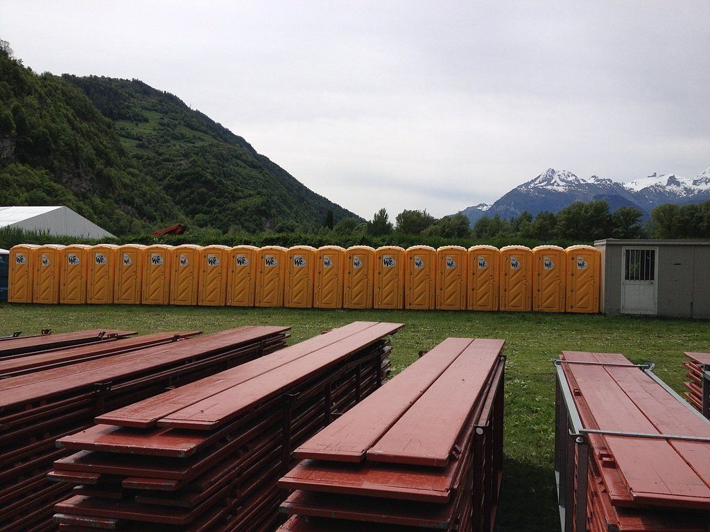 Une rangée de toilettes portables est alignée dans un champ avec des montagnes en arrière-plan.
