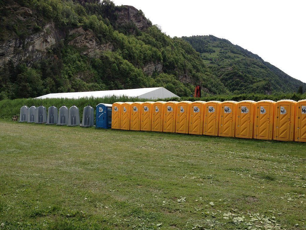 Une rangée de toilettes portables jaunes et bleues est alignée dans un champ herbeux.