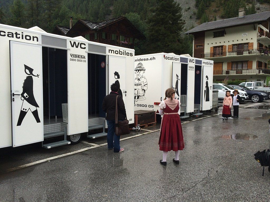 Une femme en robe rouge se tient devant une rangée de toilettes mobiles