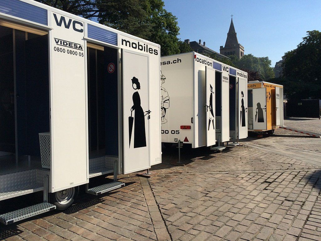 Une rangée de toilettes mobiles est garée sur un parking.