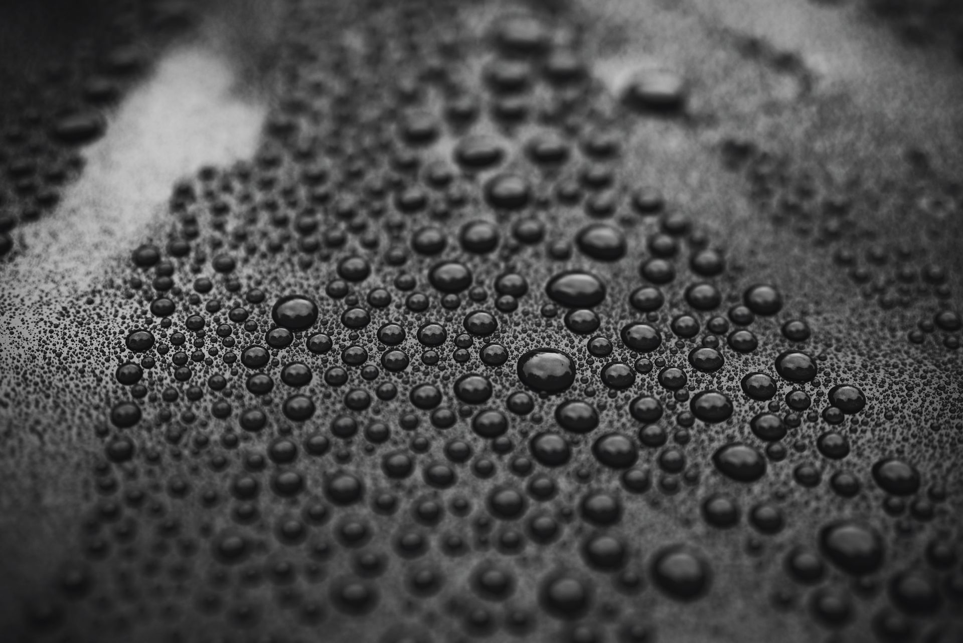 Close-up of numerous water droplets on a dark, textured surface, creating a bubble-like pattern.
