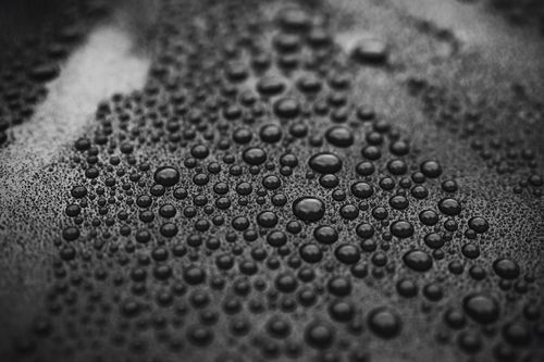 Close-up of numerous water droplets on a dark, textured surface, creating a bubble-like pattern.