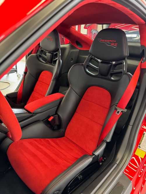 Red and black custom car interior with racing seats and safety belts.